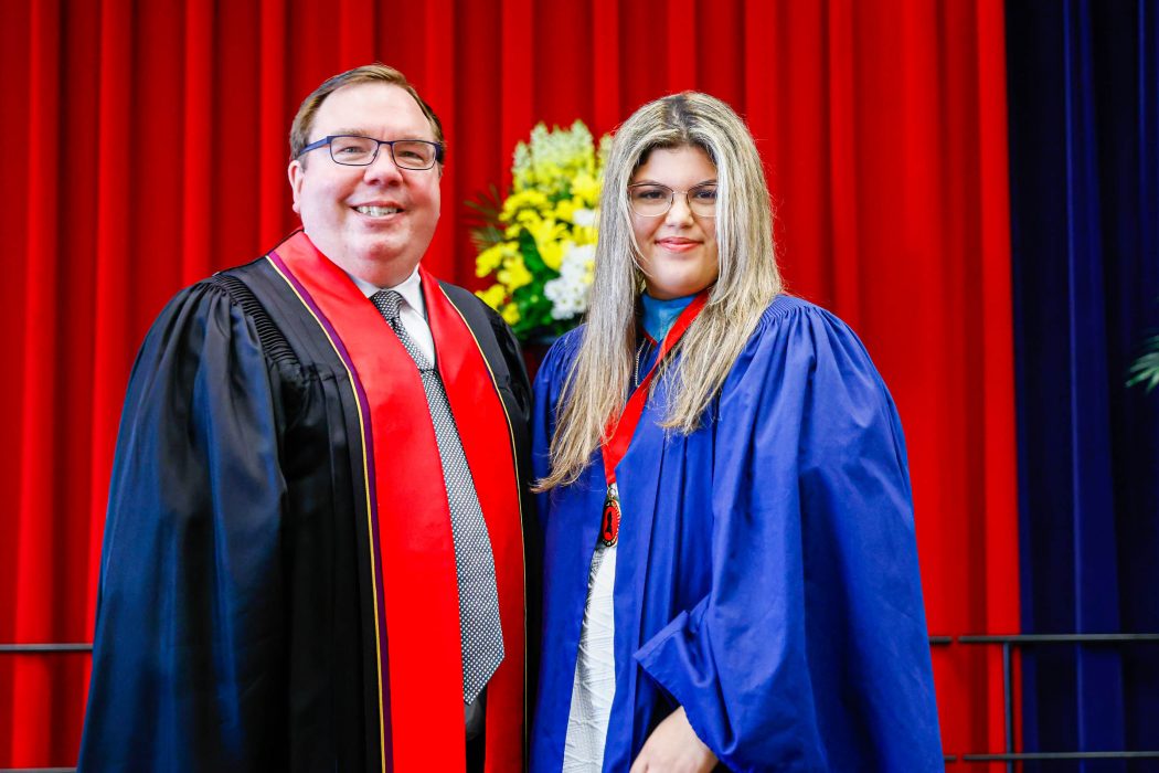 A man in academic regalia stands next to a new graduate on stage at Convocation.