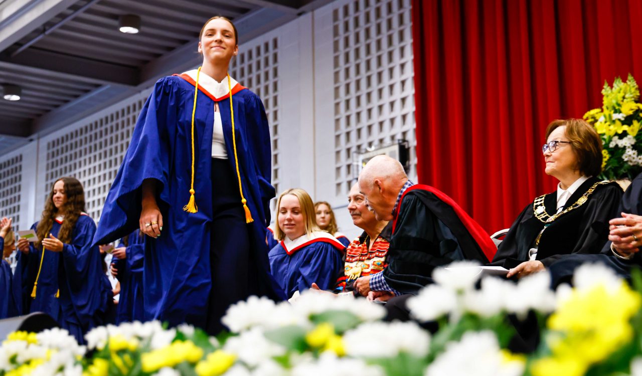 A woman walks across the stage wearing a blue gown.