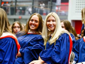 Two graduating students sit smiling during a Convocation ceremony.