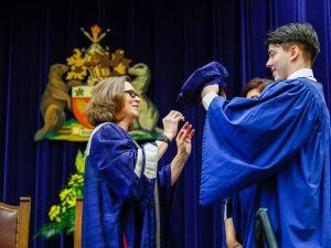 A man passes a hat to Lesley Rigg, Brock University's President and Vice-Chancellor, during her installation at Brock's graduation ceremony.