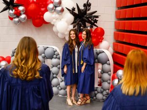 Two young women in graduation gowns pose for a photo in front of a balloon display.