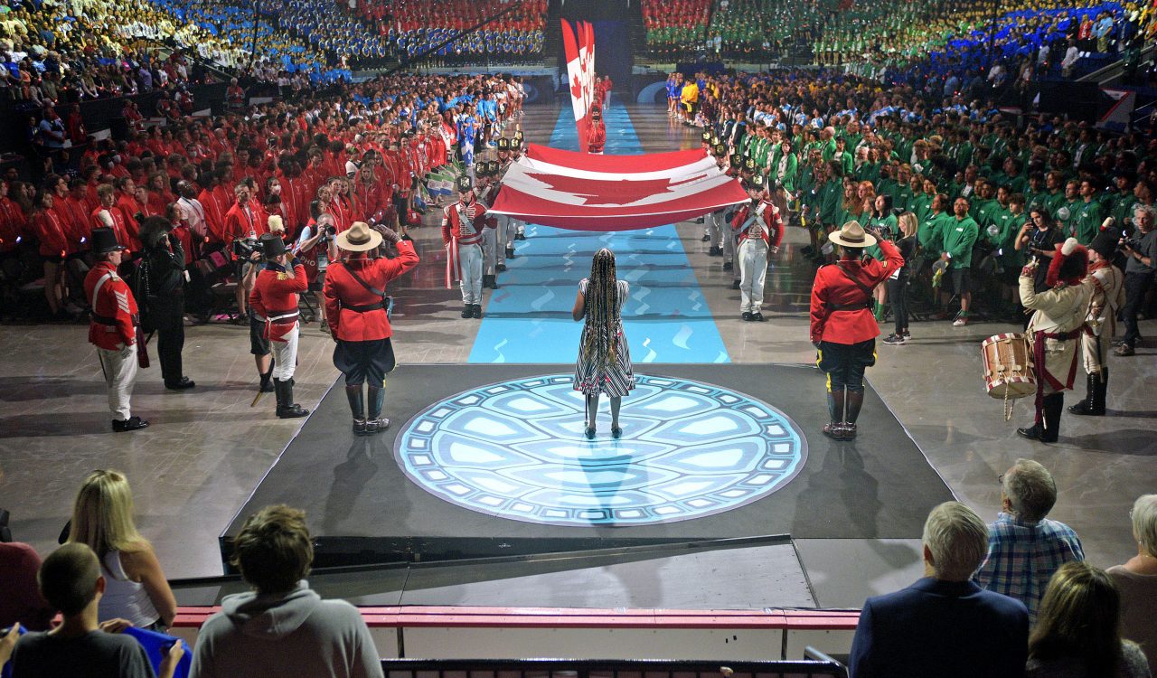 A performer stands at the centre of a stage in front of a large crowd.