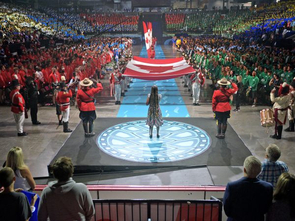 A performer stands at the centre of a stage in front of a large crowd.