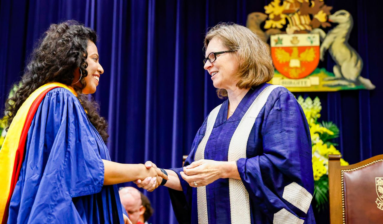 Two women in ceremonial Convocation gowns shake hands.