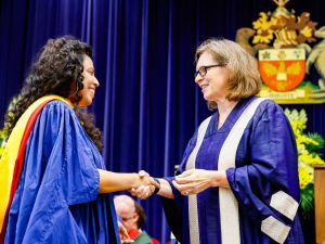 Two women in ceremonial Convocation gowns shake hands.