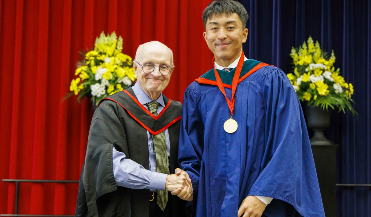 Bao (Bill) Huynh and Rob Welch shake hands on stage during Convocation.