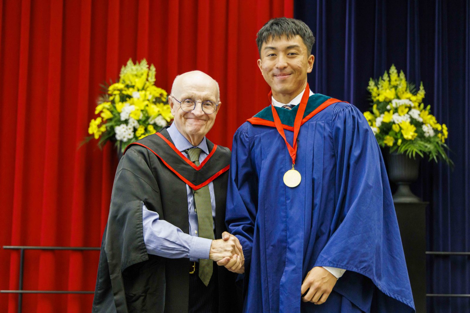 Bao (Bill) Huynh and Rob Welch shake hands on stage during Convocation.