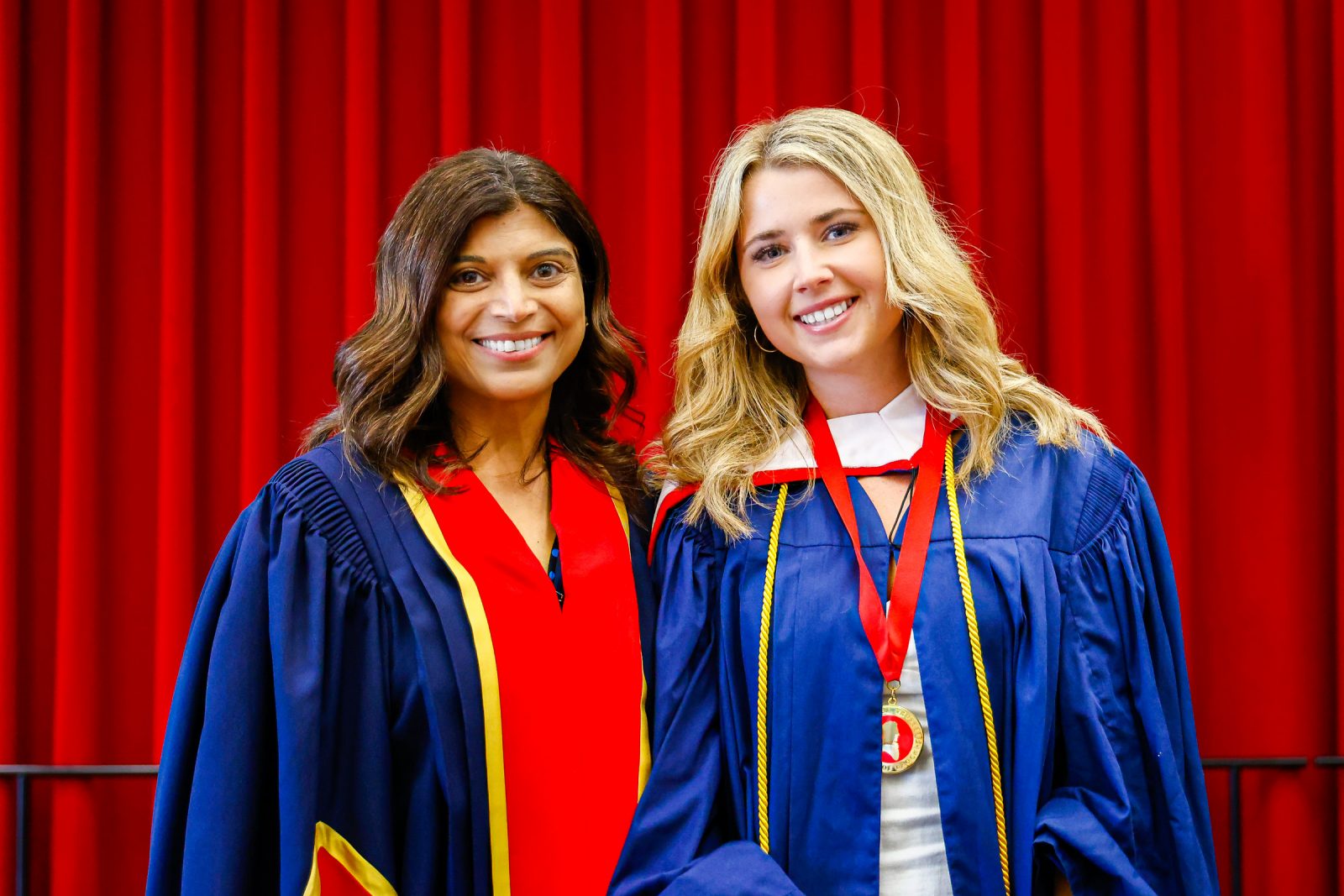 Two women stand side-by-side in academic robes.