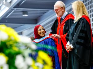 A woman in a head covering and ceremonial convocation robe receives her hood at Brock university Convocation.
