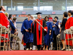 A group of people wearing academic robes proceed into a graduation ceremony.