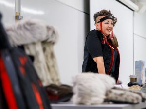 A woman stands smiling behind a table full of traditional Indigenous items.