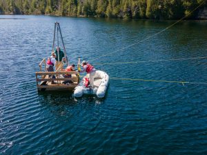 Two researchers standing, and one squatting, on a wooden raft with an inflatable dinghy with a researcher standing in it next to the raft.