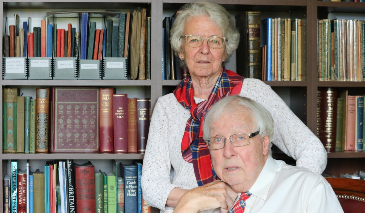 David Murray and Elizabeth Surtees pose in their personal library. Murray is wearing a Brock University tartan tie and Surtees the Brock tartan scarf.