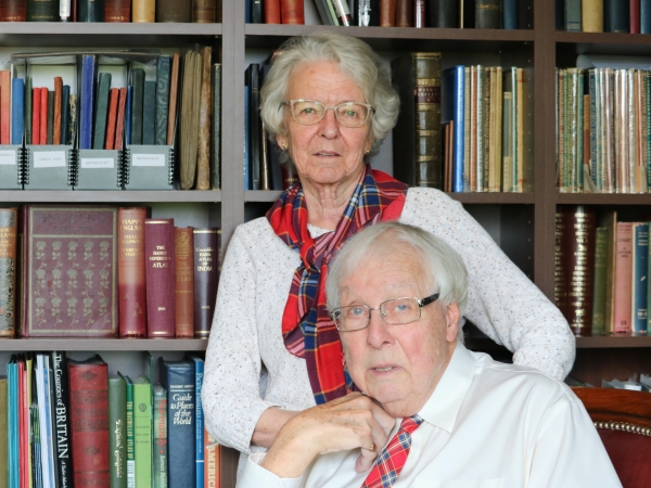 David Murray and Elizabeth Surtees pose in their personal library. Murray is wearing a Brock University tartan tie and Surtees the Brock tartan scarf.
