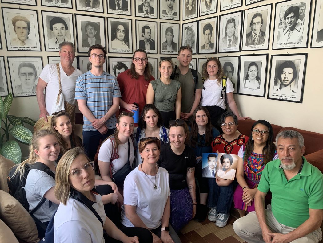Students, researchers and local experts pose in a room decorated with portraits of missing and murdered individuals.