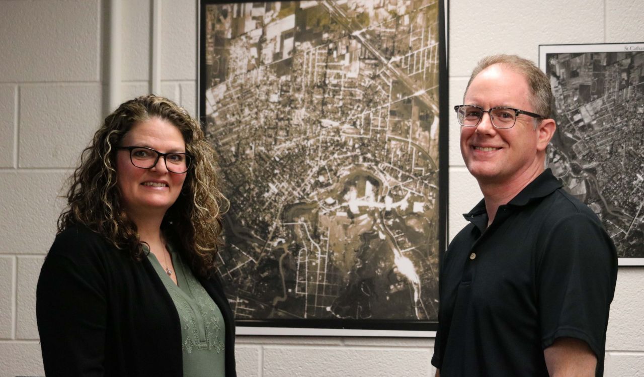 A woman and a man stand on either side of a large historical map of St. Catharines from 1934.
