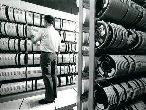 A man stands in front of a wall of old computer tapes.