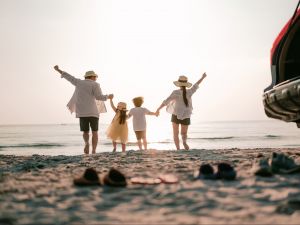 A family of four stands on the edge of a beach's shore facing the water.