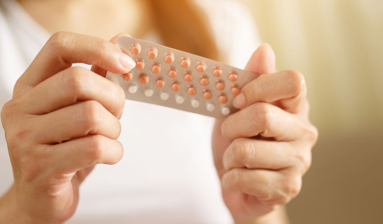 Close-up of a woman’s hands holding a birth control blister pack with orange and white pills.