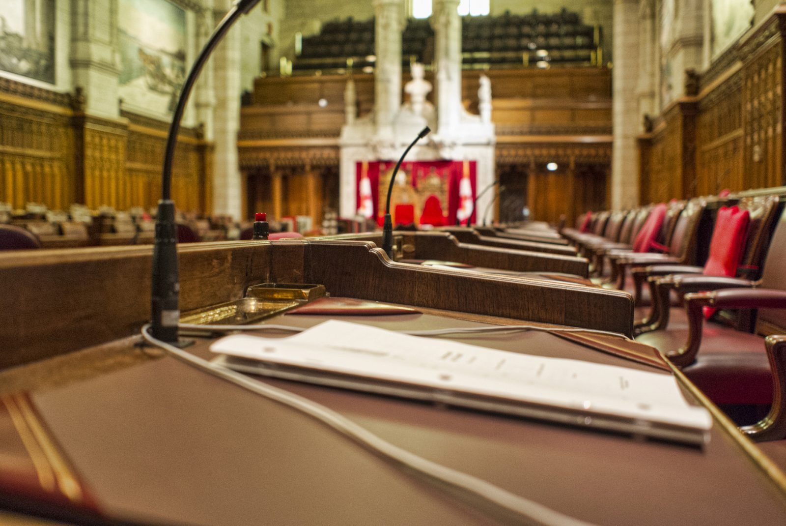 Close up of a Senator's desk with paperwork in the chambers of the Senate of Canada. The Speaker's chair can be seen in the background.