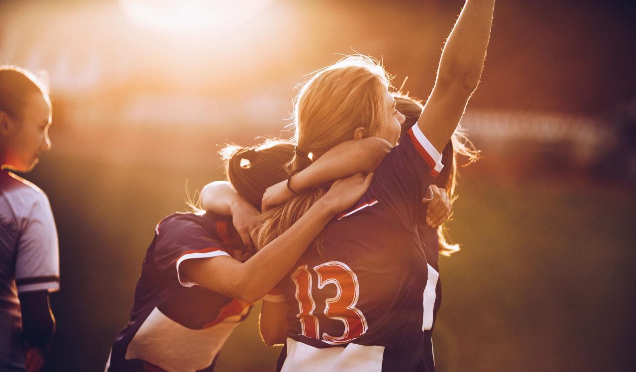 Team of happy female soccer players celebrating their achievement on a playing field at sunset.