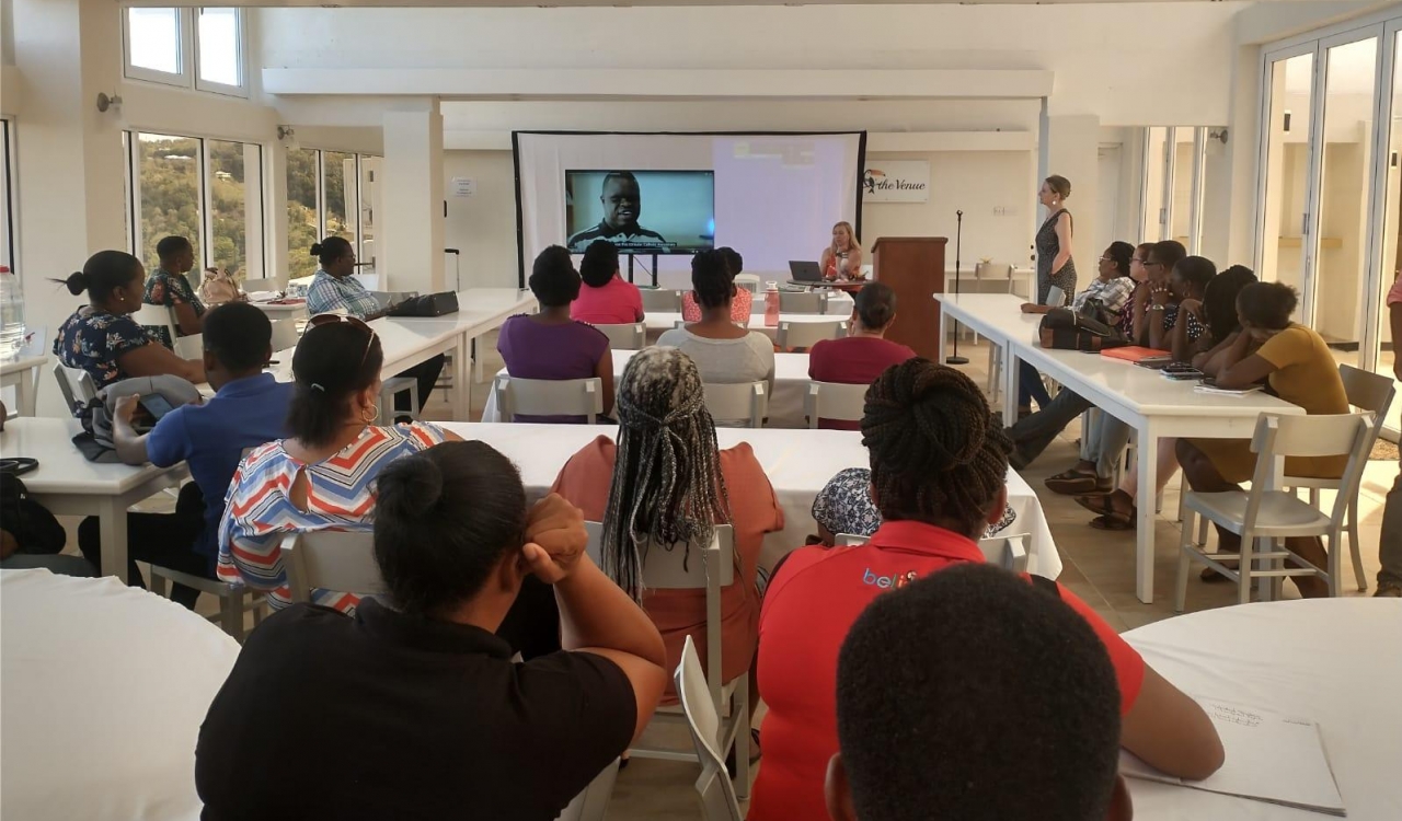 A group of people watch a video on a screen at the front of a room during a training session.
