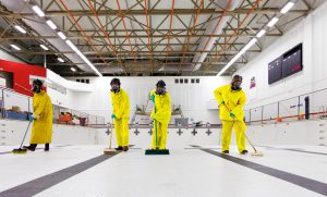 Workers wearing protective clothing and masks clean an empty indoor pool.