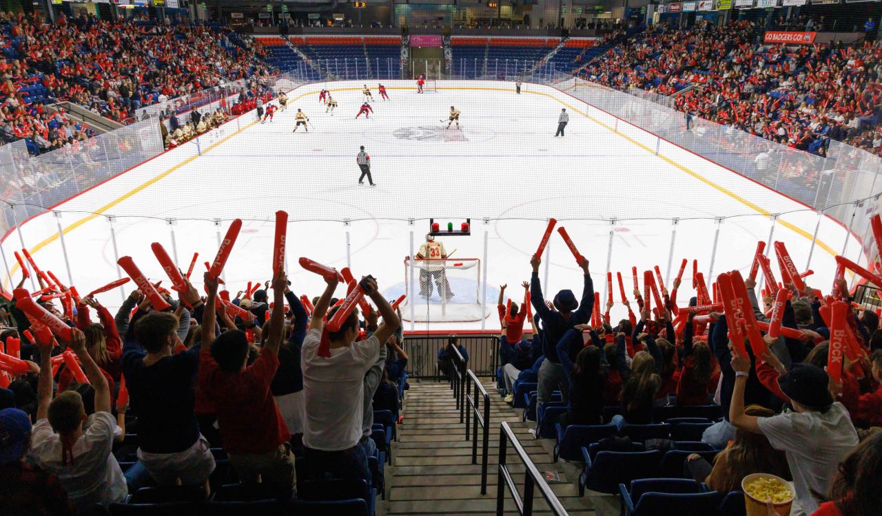 A large crowd cheers on a hockey game inside of an arena.