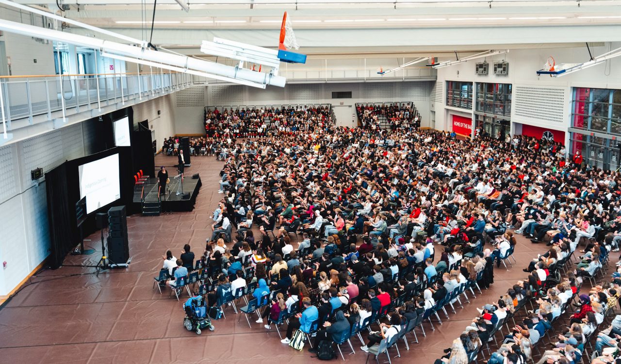 An aerial photo of a gymnasium full of seated university students.
