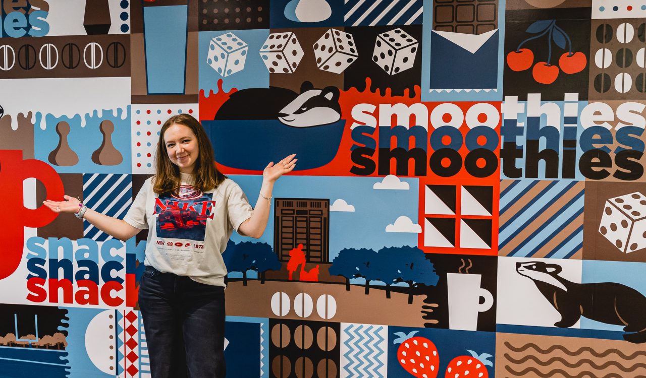 A young woman stands in front of a colourful mural painted on a wall.