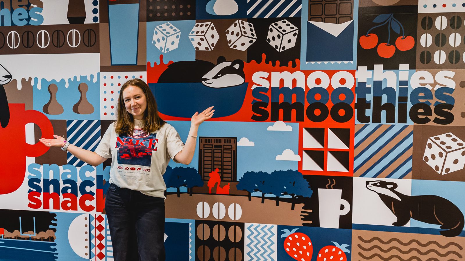 A young woman stands in front of a colourful mural painted on a wall.