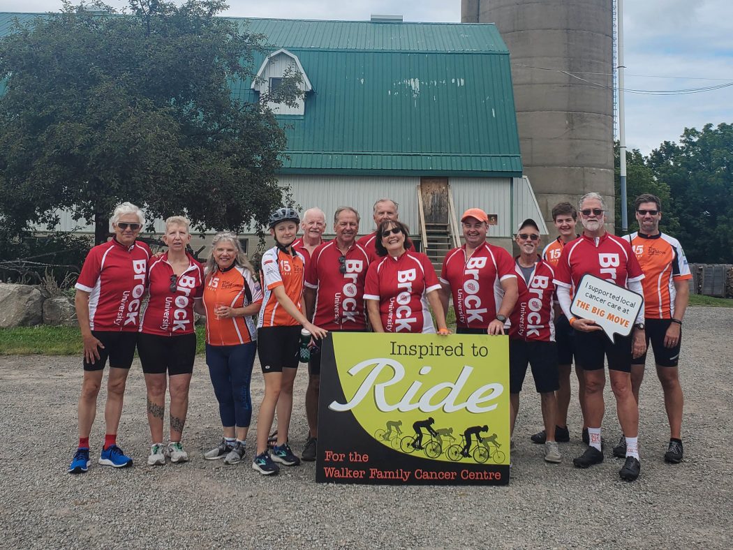 A team of people in red or orange cycling uniforms poses for a photo at charity cycling event.