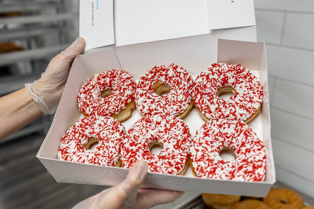 A box of six doughnuts with red and white sprinkles.