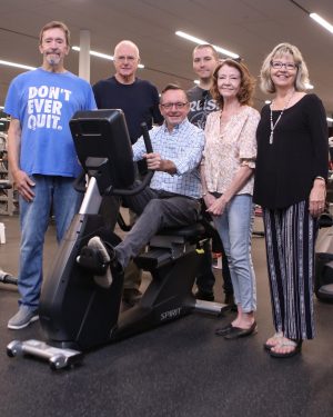 Rick Page sits on an exercise bike in the Brock Functional Inclusive Training Centre while five of his family members stand around him to pose for a photo.