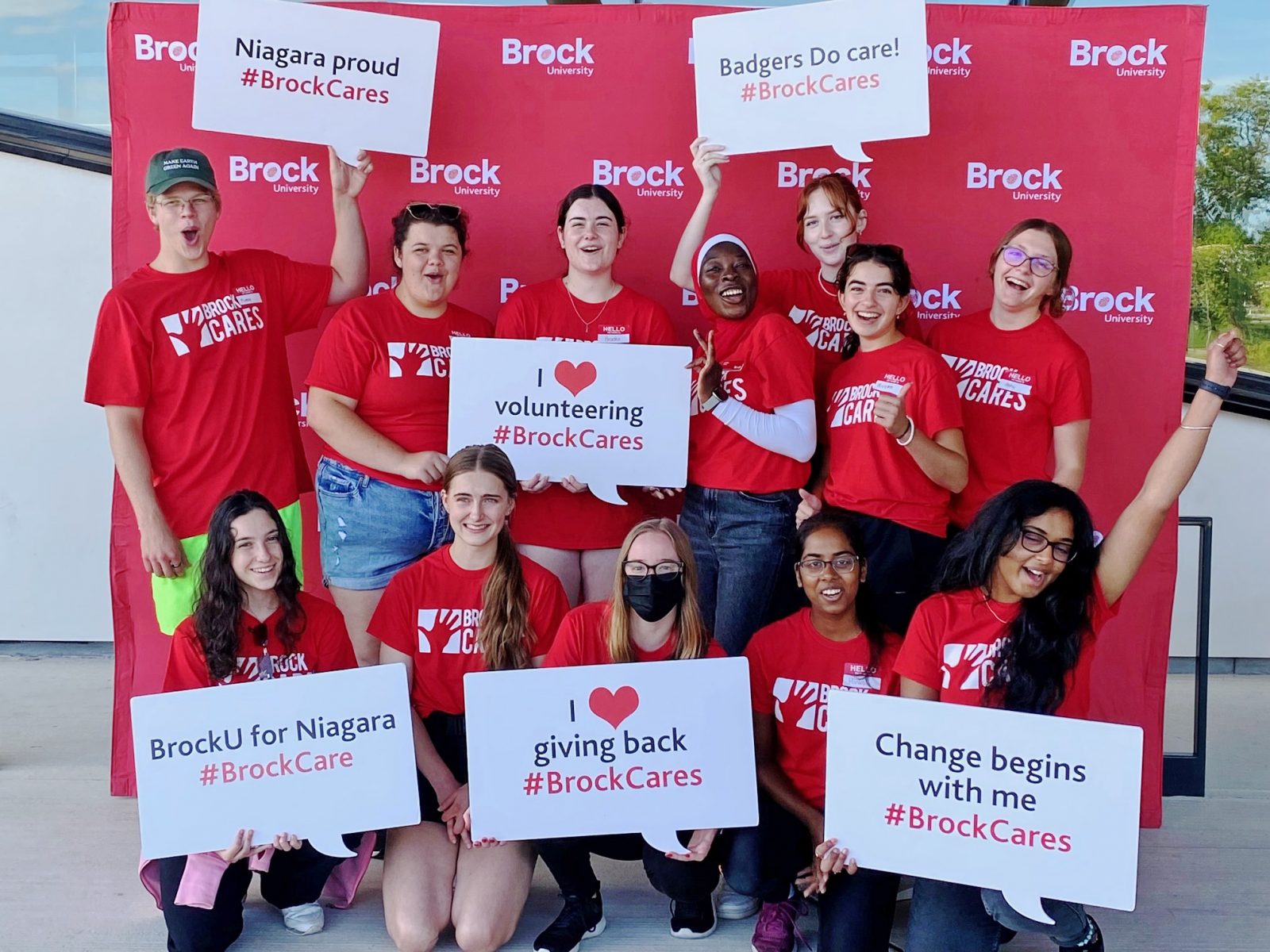 A group of 12 students wearing Brock Cares t-shirts hold signs with Brock Cares messages.