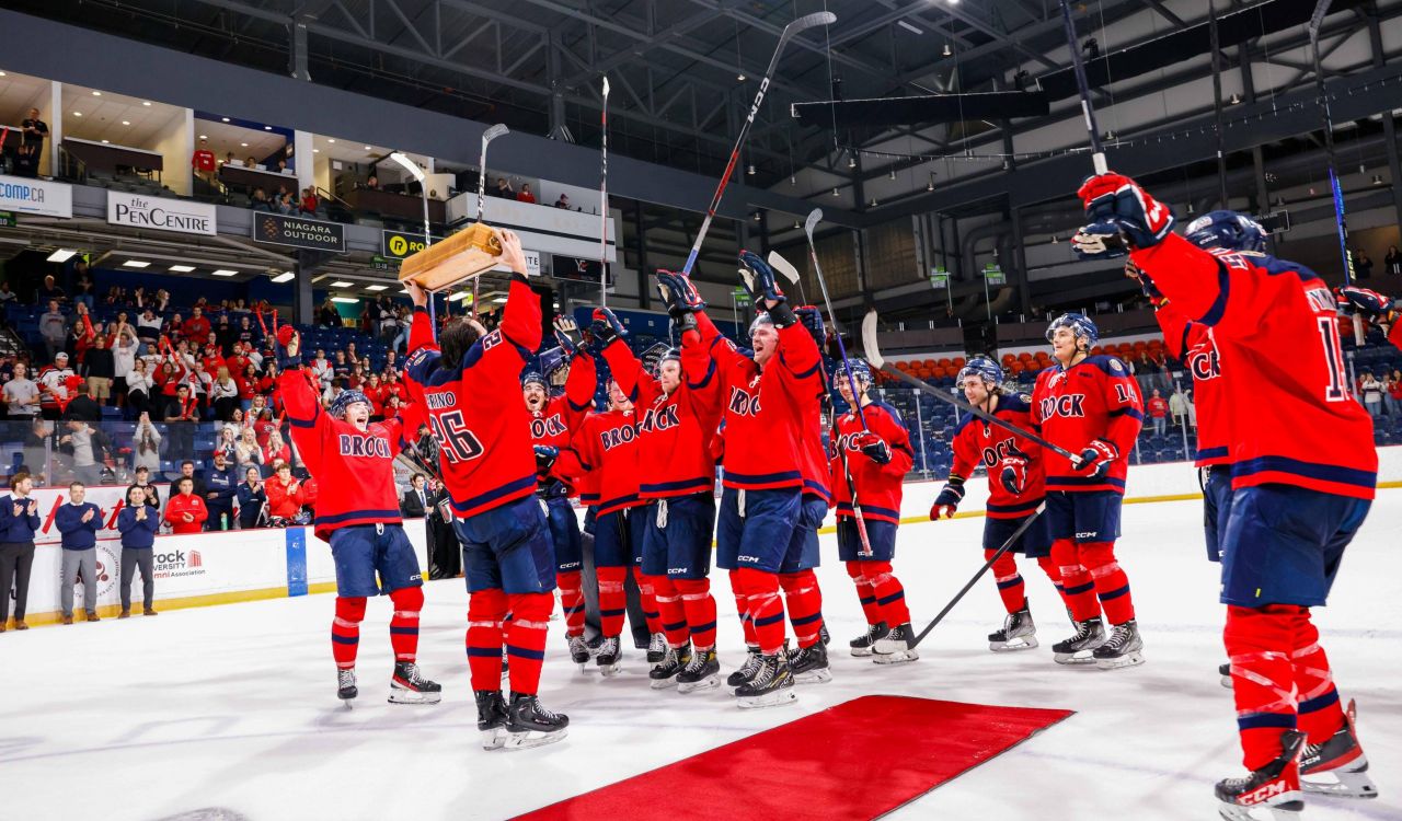 A team of hockey players celebrates a victory on the ice of an indoor arena. 