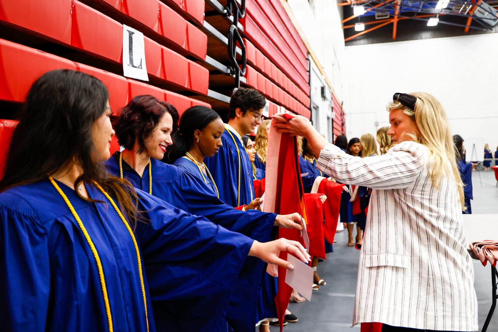 A woman passes out academic hoods to a row of people in university graduation gowns.