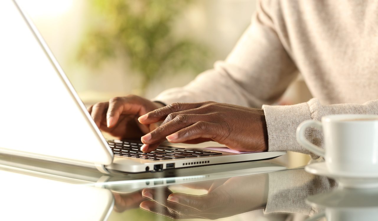 Close up of man's hands typing on a laptop sitting on a desk at home.