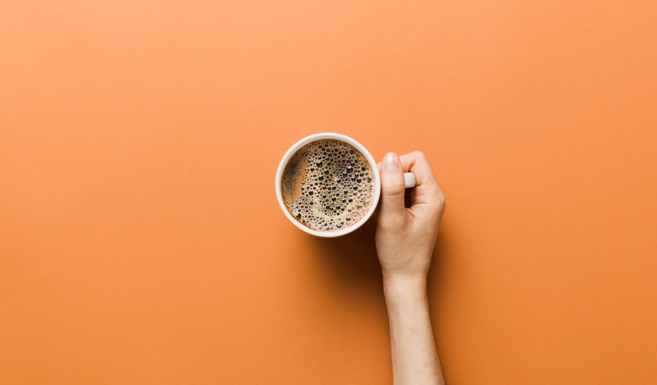 A woman's hand holding a cup of coffee over an orange background.