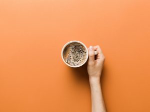 A woman's hand holding a cup of coffee over an orange background.