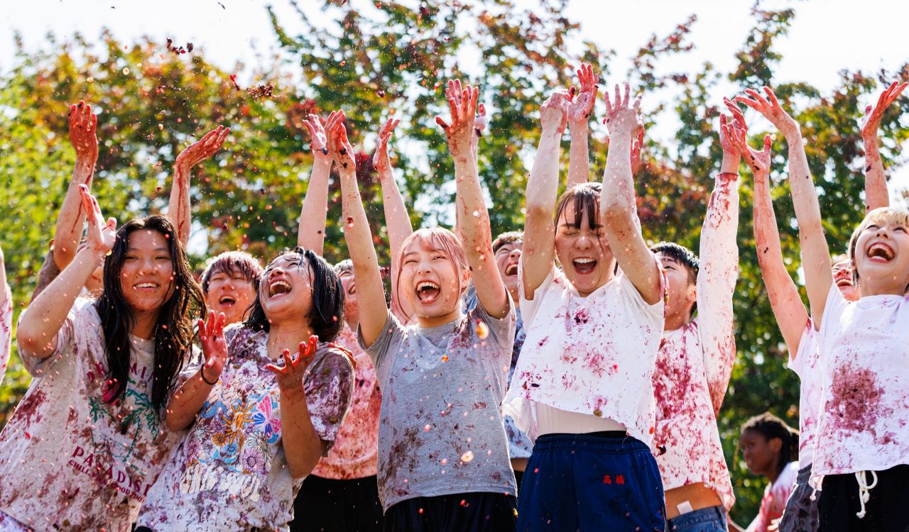 A group of women covered in grape juice toss grapes into the air.