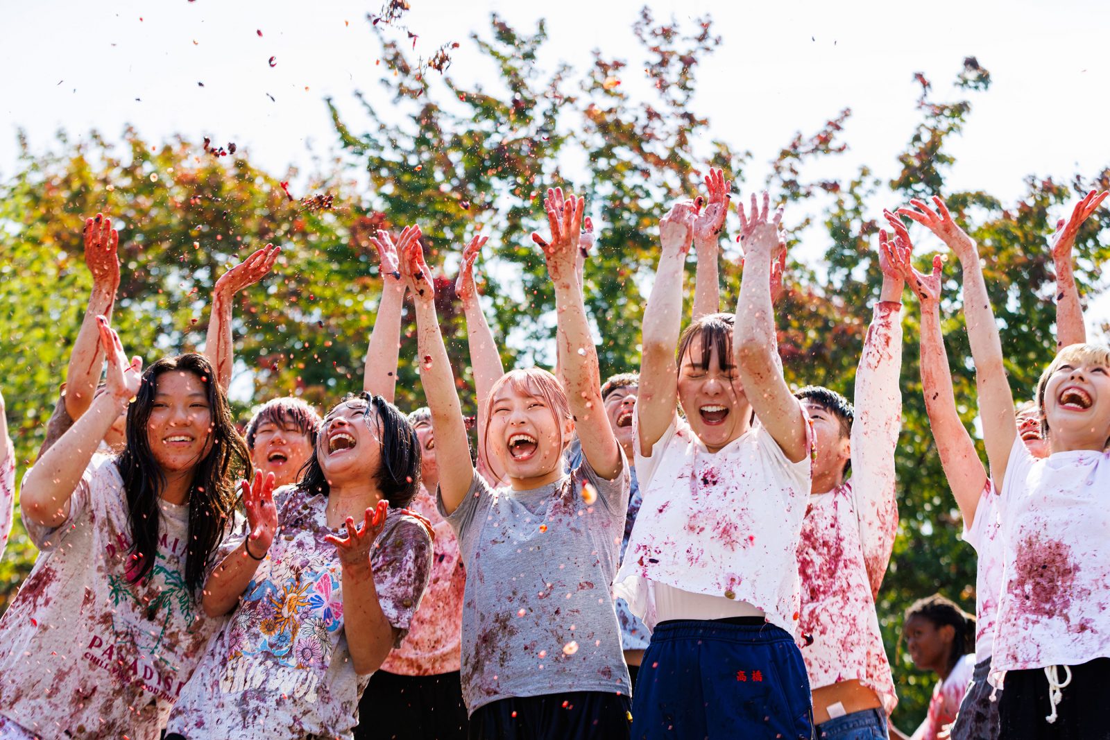A group of women covered in grape juice toss grapes into the air.