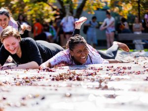 Two women slides through a mess of grapes on a tarp outdoors.