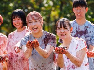 A group of women hold a handful of messy grapes forward.