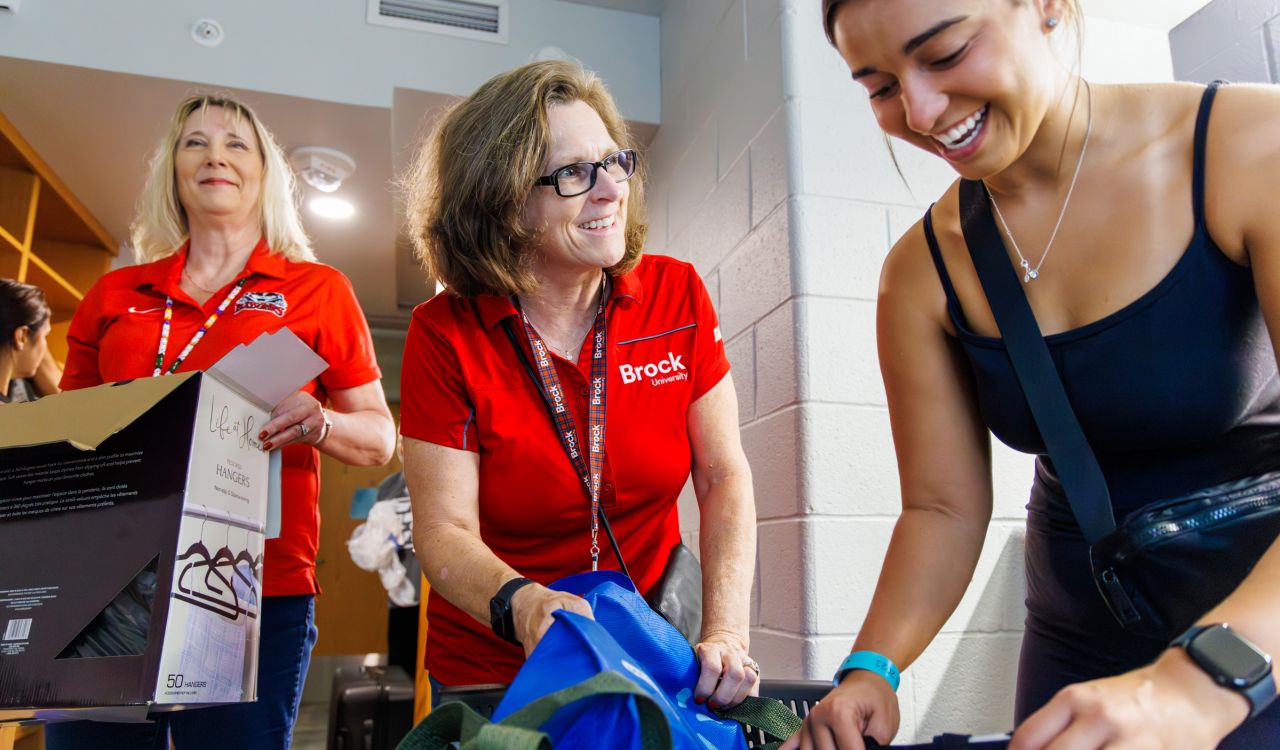 Three women unpack luggage in a university dorm room.
