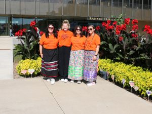 A group of women in orange shirts stands next to a garden.