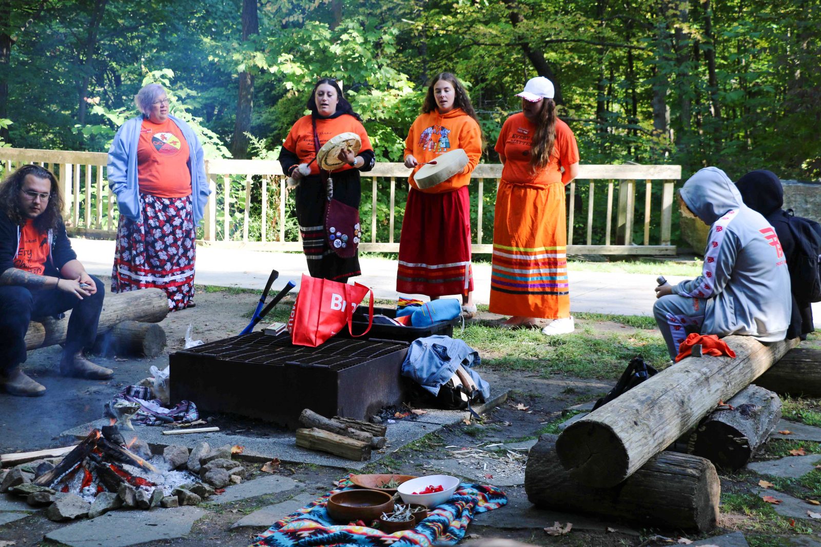 A group of people participate in a ceremony beside a firepit.