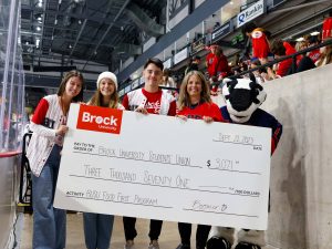Four people and a badger mascot stand holding a giant cheque for the Brock University Students' Union Food First program totalling $3,071.