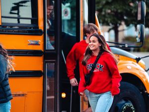 Two people in Brock branded sweatshirts walk in front of a yellow school bus.