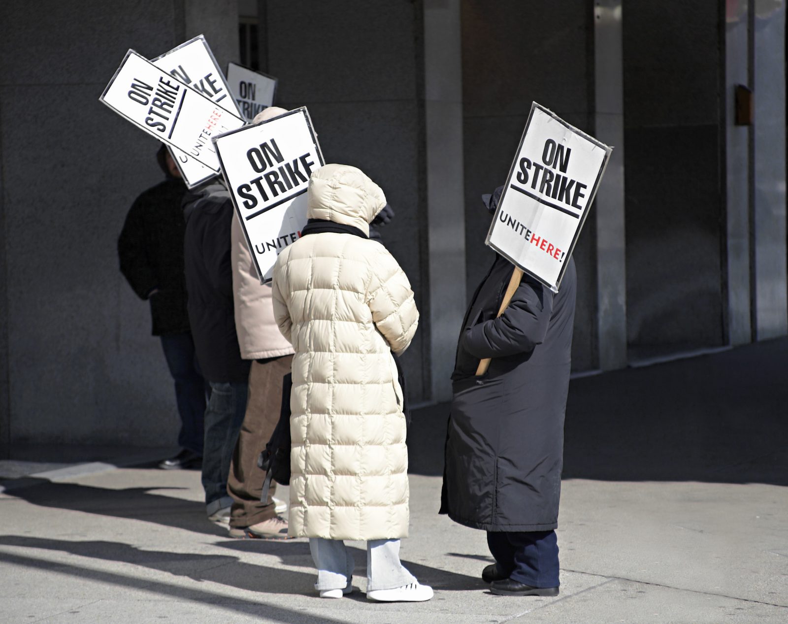 Workers stand outside holding picket signs next to a building.